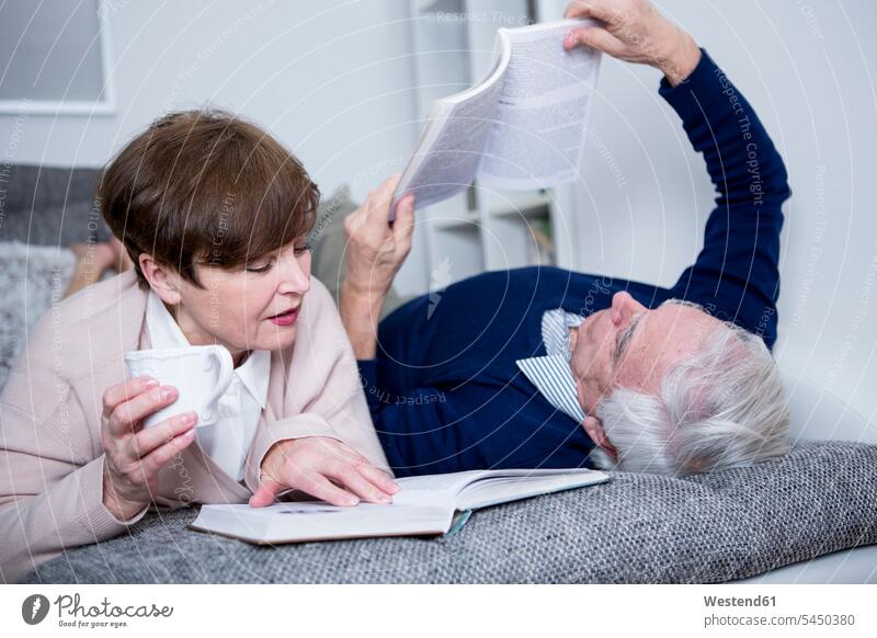 Senior couple lying on couch, reading books laying down lie lying down Coffee settee sofa sofas couches settees twosomes partnership couples senior adults