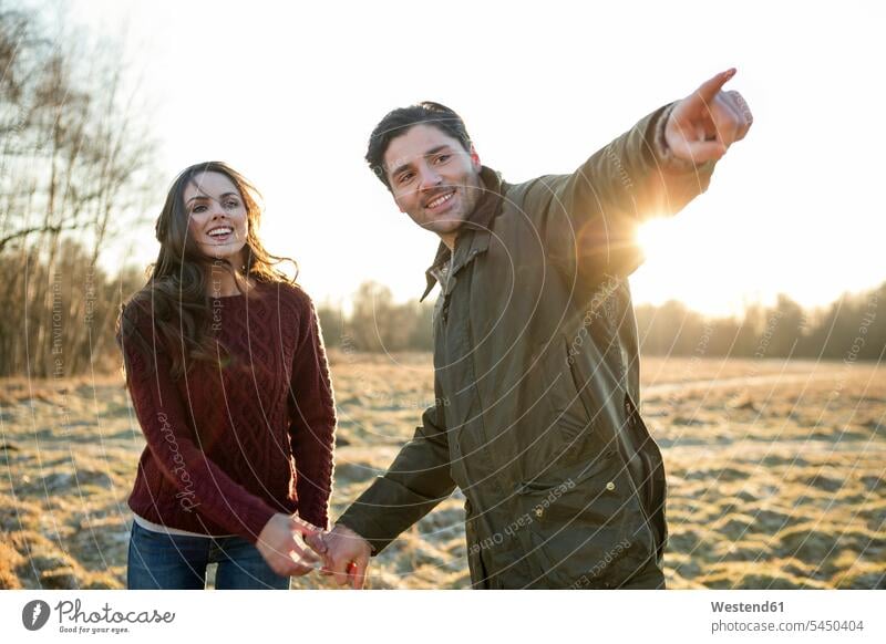 Young couple taking a walk in evening sun twosomes partnership couples autumnal autumnally pointing point at pointing at show showing sunset sunsets sundown