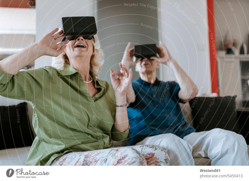 Happy senior couple at home sitting on couch wearing VR glasses settee sofa sofas couches settees twosomes partnership couples Virtual Reality Glasses