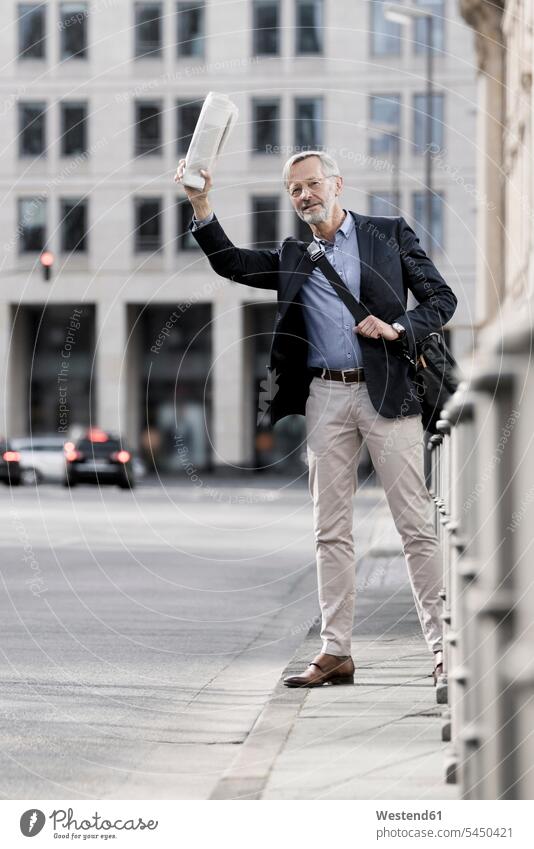 Grey-haired businessman with newspaper calling a taxi in the city roadside Road Side waving wave Businessman Business man Businessmen Business men standing