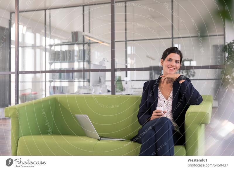 Businesswoman with laptop sitting on a couch and drinking coffee in the office smartwatch smart watch working At Work Internet The Internet using laptop