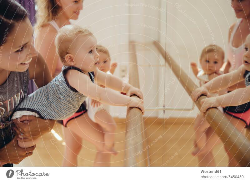 Two mothers holding up their small children to barre in dance studio mommy mummy mama mirror mirrors baby infants nurselings babies smiling smile Fun having fun