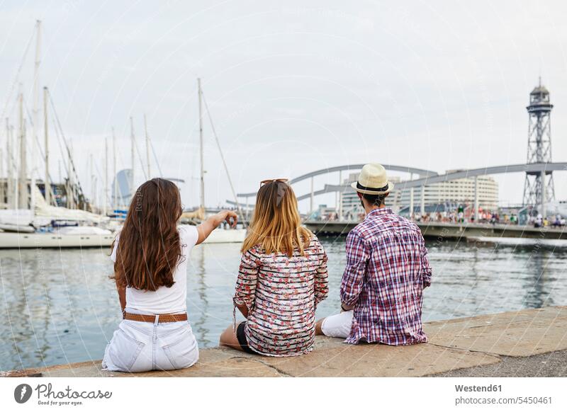 Spain, Barcelona, three tourists sitting on a pier in the city friends mate piers tourism touristic friendship water's edge waterside shore urban urbanity