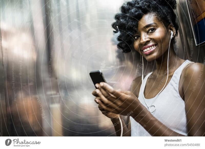 Portrait of happy woman with cell phone and earphones in underground train Smartphone iPhone Smartphones females women portrait portraits mobile phone mobiles