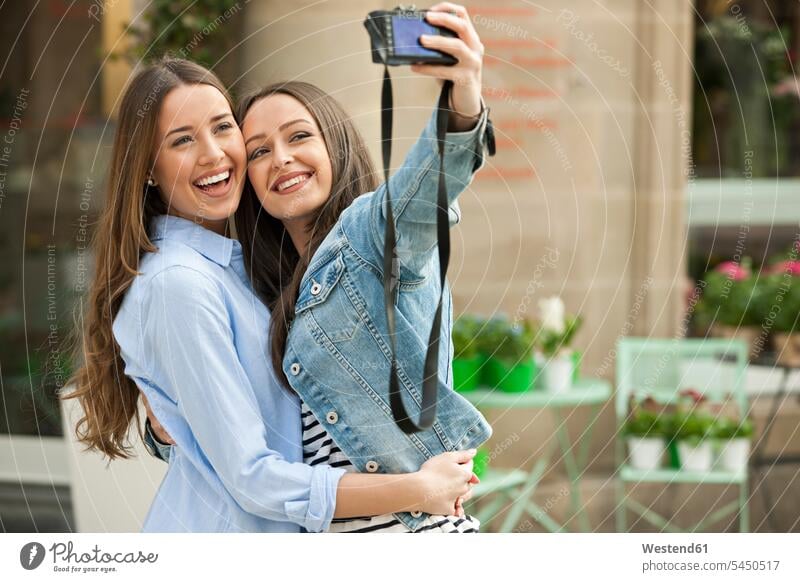 Laughing girlfriends taking a selfie in the street Selfie Selfies photographing laughing Laughter camera cameras female friends together positive Emotion