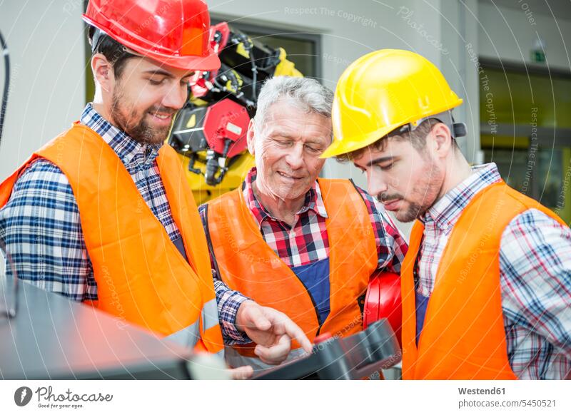 Three men in factory talking with industrial robot in background factories working At Work Robot industry occupation profession professional occupation jobs