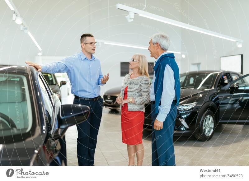 Senior couple couple talking with salesperson in car dealership twosomes partnership couples automobile Auto cars motorcars Automobiles advising counseling
