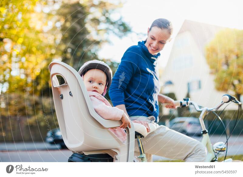 Mother and daughter riding bicycle, baby wearing helmet sitting in children's seat bikes bicycles Child's Seat child seat child safety seat riding bike