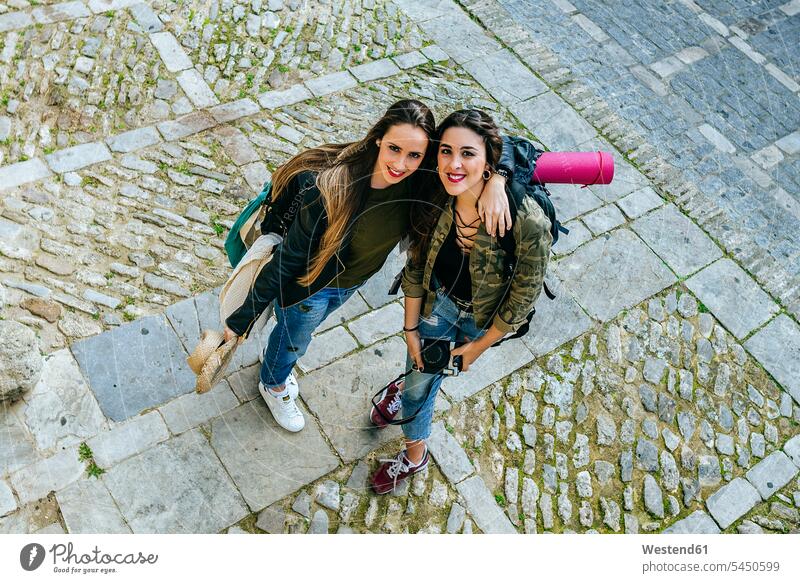 Two traveling young women standing on tow square smiling smile female friends mate friendship embracing embrace Embracement hug hugging camera cameras woman