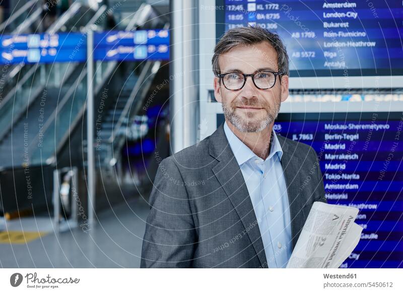 Smiling businessman with newspaper at timetable at the airport smiling smile terminal airports Businessman Business man Businessmen Business men transportation