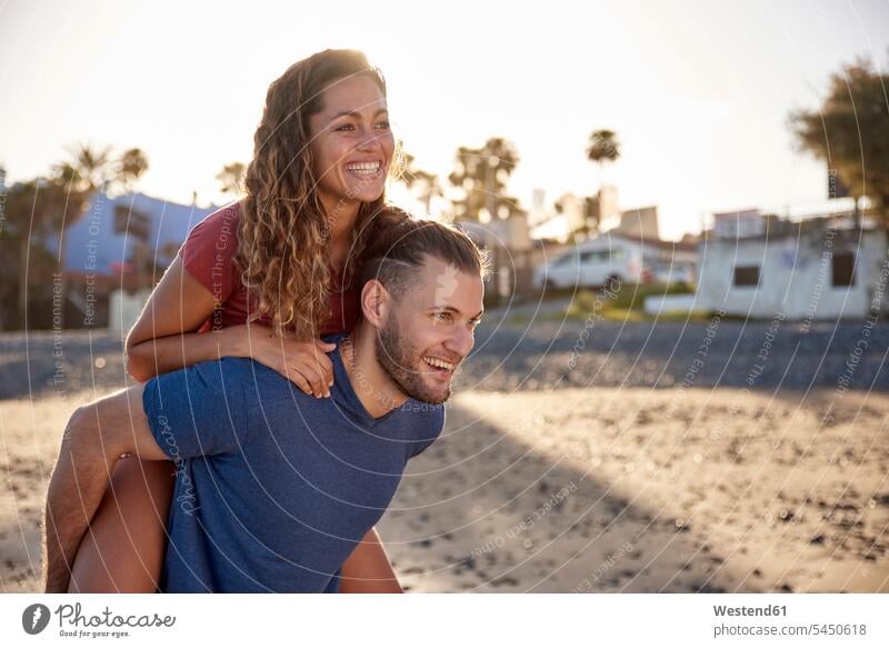 Young man giving his girlfriend a piggyback ride on the beach couple twosomes partnership couples piggy-back pickaback Piggybacking Piggy Back beaches people
