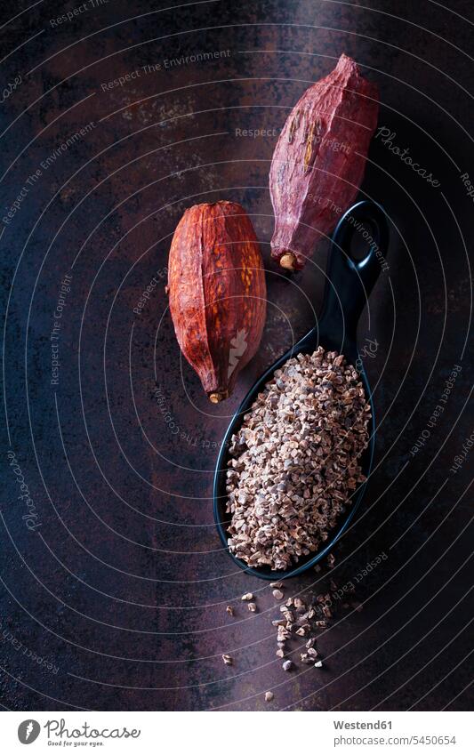 Spoon of crushed raw cacao nibs and cacao pods on rusty metal brown healthy eating nutrition crushing dried cocoa pod cocoa pods dark background vegan superfood