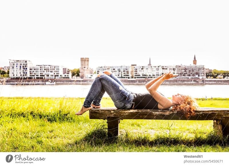 Germany, Cologne, redheaded young woman lying on bench taking selfie with cell phone Selfie Selfies females women laying down lie lying down Adults grown-ups