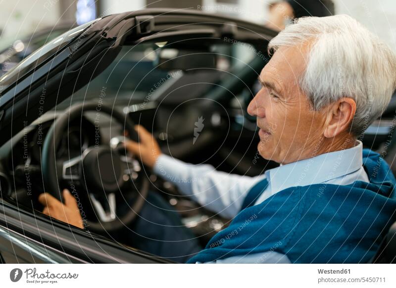 Senior man testing convertible in car dealership automobile Auto cars motorcars Automobiles choosing select choose selecting customer clientele clients