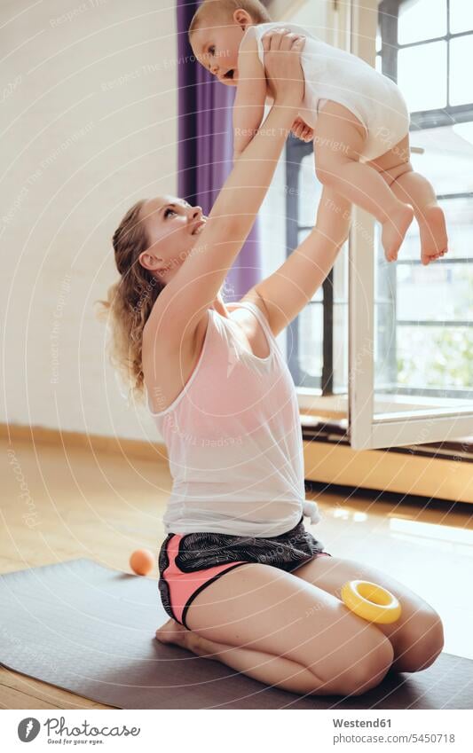 Mother holding up her baby while working out on a yoga mat exercising exercise training practising Fun having fun funny mother mommy mothers mummy mama infants
