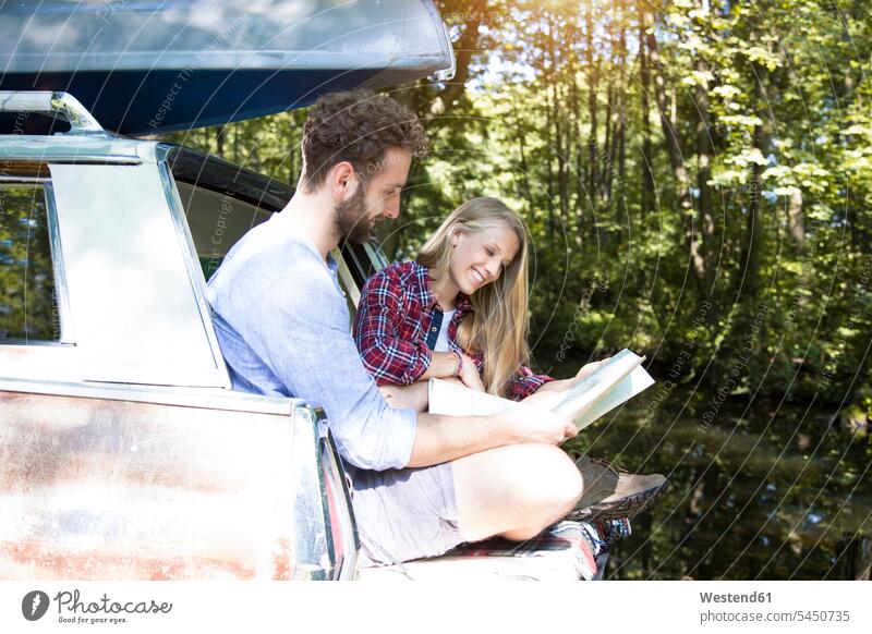 Smiling young couple with map and canoe in car at a brook maps brooks rivulet forest woods forests smiling smile automobile Auto cars motorcars Automobiles
