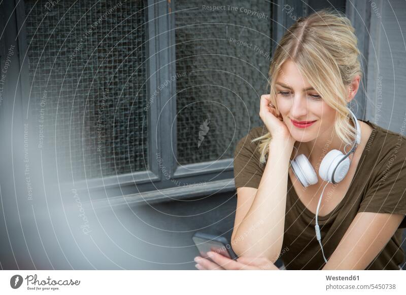 Relaxed young woman with headphones looking at cell phone Smartphone iPhone Smartphones females women mobile phone mobiles mobile phones Cellphone cell phones