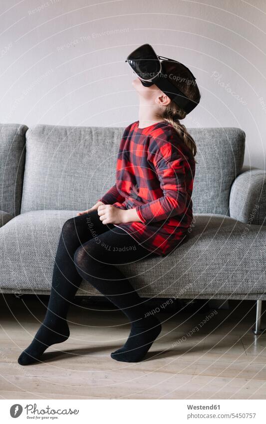 Girl sitting on the couch in the living room using Virtual Reality Glasses settee sofa sofas couches settees living rooms livingroom use Seated VR glasses