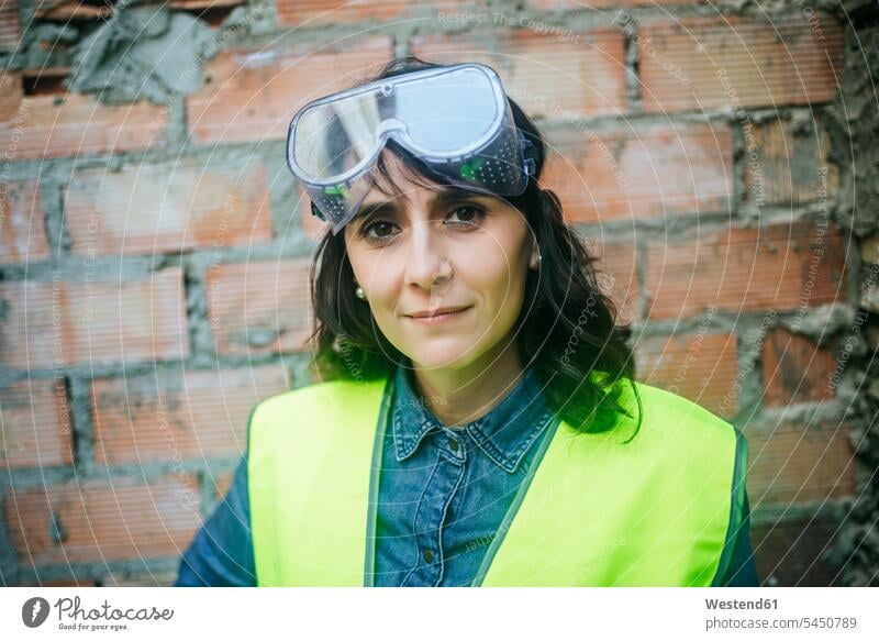 Portrait of confident woman wearing safety glasses on construction site portrait portraits working At Work females women Building Site sites Building Sites