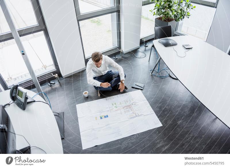 Businessman sitting on the floor of his office looking at construction plan Business man Businessmen Business men offices office room office rooms