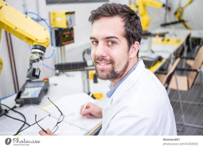 Portrait of smiling engineer in factory taking notes factories smile Robot engineers technology technologies engineering industry industrial examining checking