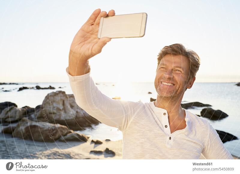 Portrait of smiling man taking selfie on the beach with cell phone Sea ocean men males Selfie Selfies water Adults grown-ups grownups adult people persons