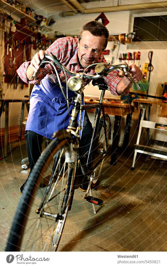Senior man checking bicycle in his workshop bikes bicycles senior men senior man elder man elder men senior citizen craft crafts handwork handcraft hand work