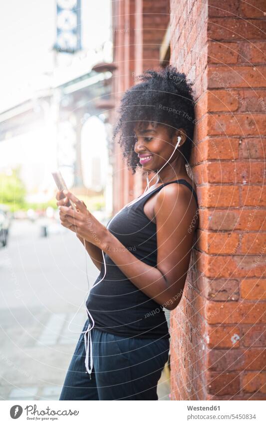 USA, New York City, Brooklyn, smiling woman leaning against brick wall listening to music smile hearing females women Adults grown-ups grownups adult people