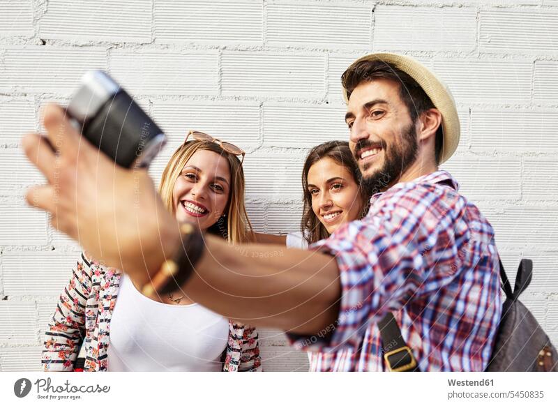 Three friends taking photos at white wall mate smiling smile camera cameras Selfie Selfies friendship walls together positive laughing Laughter Spain relaxation