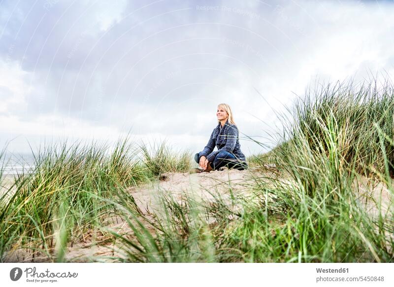 Smiling woman sitting in dunes sand dune sand dunes Seated females women smiling smile beach beaches Adults grown-ups grownups adult people persons human being
