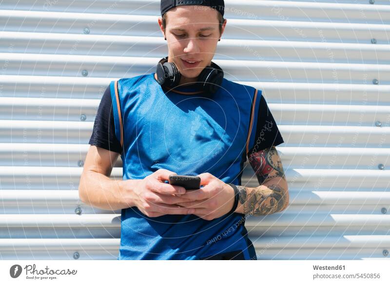 Tattooed young man with headphones looking at cell phone men males Smartphone iPhone Smartphones Adults grown-ups grownups adult people persons human being