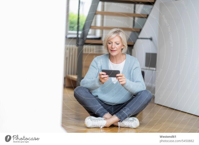 Portrait of senior woman sitting on the floor at home using smartphone Smartphone iPhone Smartphones portrait portraits females women Seated Floor Floors