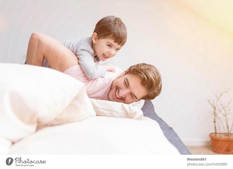 Happy father and son playing in bed beds pa fathers daddy dads papa sons manchild manchildren smiling smile parents family families people persons human being