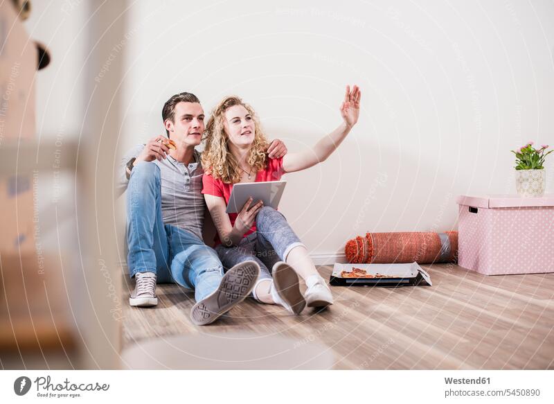 Young couple in new home sitting on floor with tablet twosomes partnership couples flat flats apartment apartments people persons human being humans