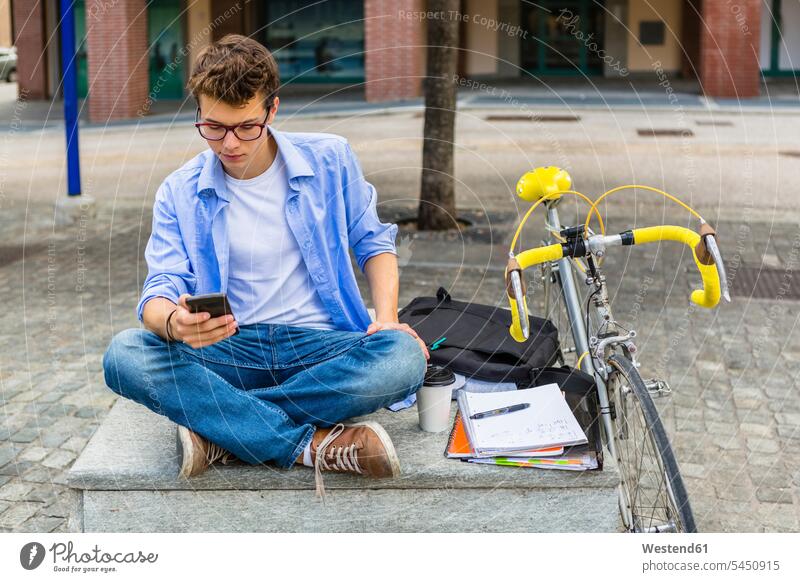 Young man with racing cycle sitting on bench looking at cell phone student students reading bicycle bikes bicycles men males University Student