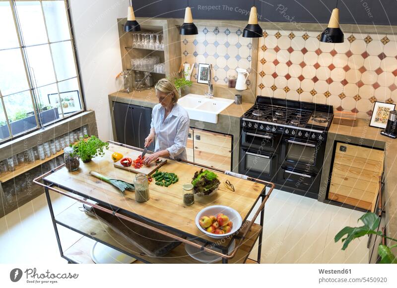 Mature woman chopping bell pepper in kitchen females women domestic kitchen kitchens Adults grown-ups grownups adult people persons human being humans