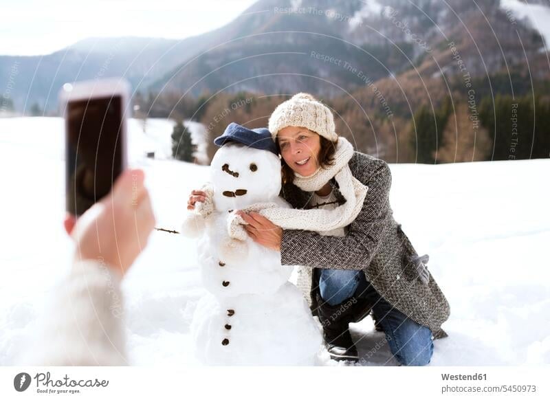 Senior man taking picture of his wife with snowman snowmen woman females women Adults grown-ups grownups adult people persons human being humans human beings