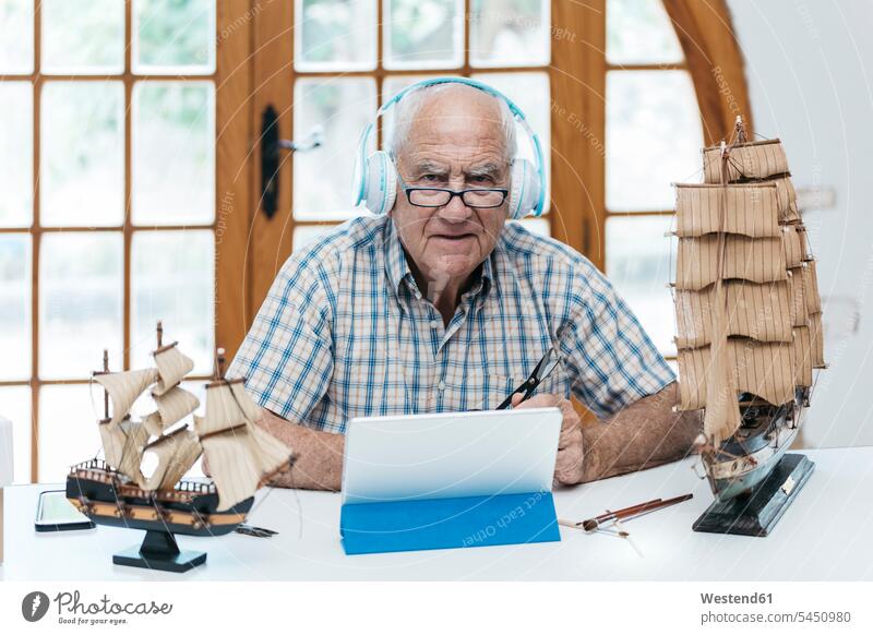 Portrait of confident senior man wearing headphones with tablet and model ship on table model boat headset digitizer Tablet Computer Tablet PC Tablet Computers