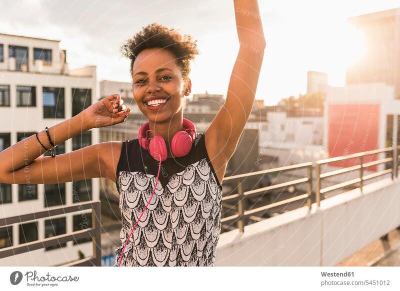 Portrait of happy young woman with headphones on rooftop smiling smile headset females women celebrating celebrate partying roof terrace deck Fun having fun