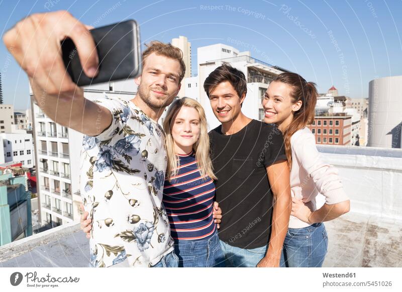 Friends taking selfies on a rooftop terrace smiling smile roof terrace deck photographing celebrating celebrate partying camera cameras Selfie Selfies friends