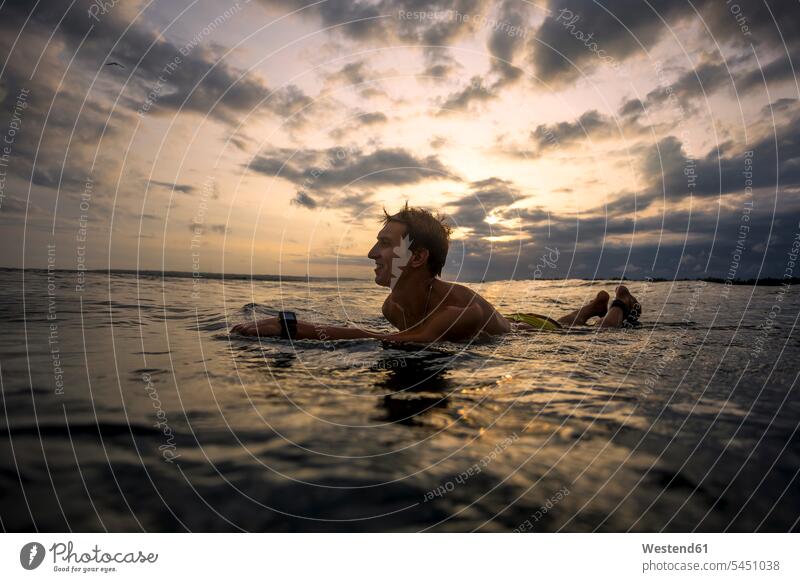Indonesia, Bali, surfer lying on surfboard at sunset Sea ocean surfers surfing surf ride surf riding Surfboarding water water sports Water Sport aquatics