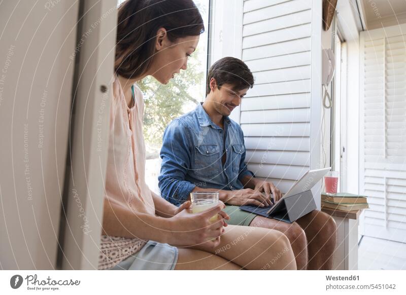 Young couple sitting on windowsill with drink and tablet relaxed relaxation smiling smile twosomes partnership couples Seated digitizer Tablet Computer