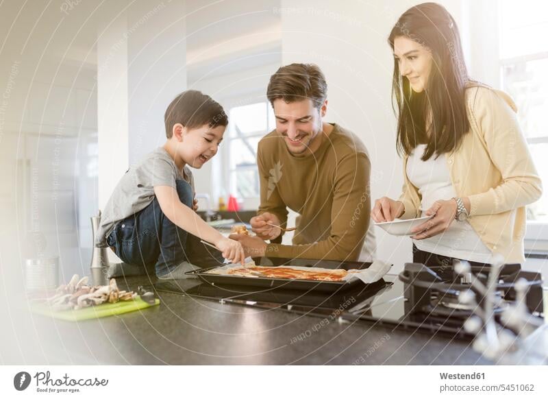 Family preparing pizza in kitchen together son sons manchild manchildren Pizza Pizzas family families smiling smile domestic kitchen kitchens cooking father
