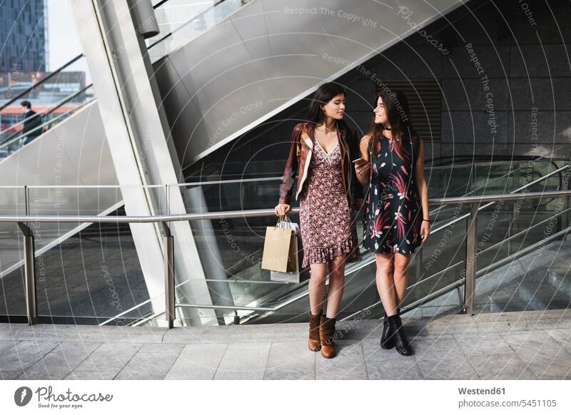Two young women with shopping bags and cell phone in the city smiling smile mobile phone mobiles mobile phones Cellphone cell phones female friends telephones