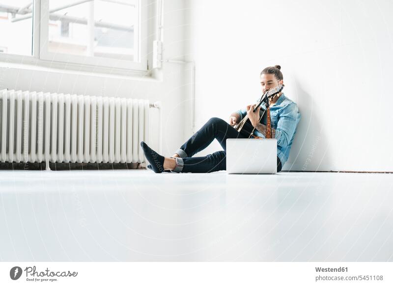 Man sitting with laptop on floor playing guitar man men males guitars Laptop Computers laptops notebook Adults grown-ups grownups adult people persons