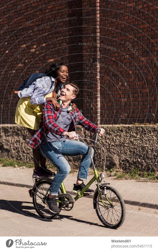 Young man riding bicycle with his girlfriend standing on rack active riding bike bike riding cycling bicycling pedaling young multicultural together headphones