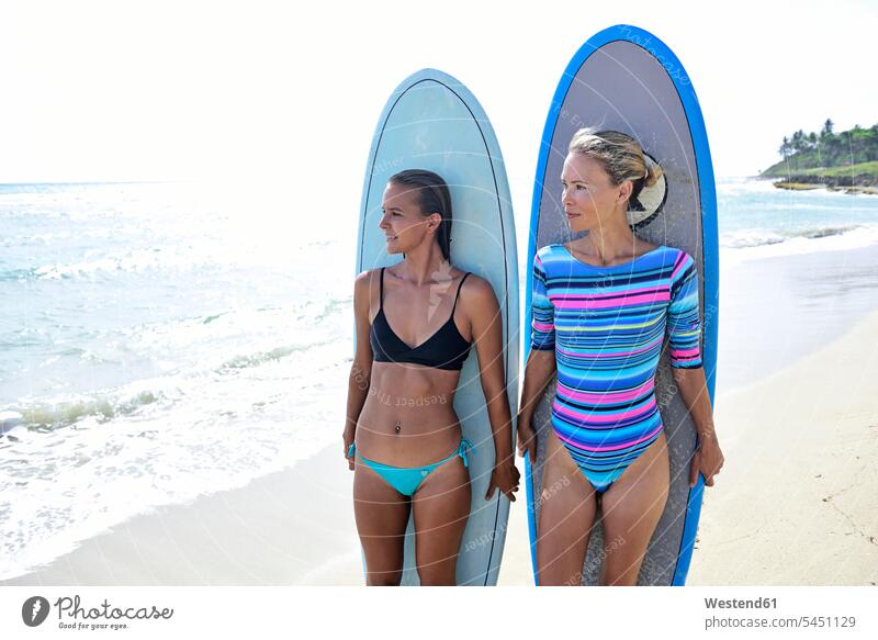 Two women on the beach with surfboards female friends standing woman females surfing surf ride surf riding Surfboarding beaches water sports Water Sport