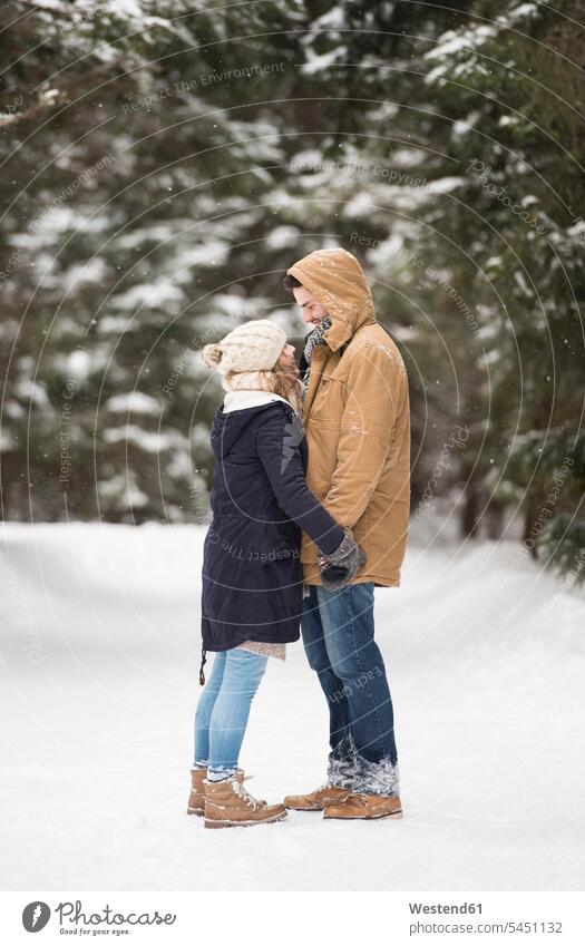 Happy young couple standing face to face in snow-covered winter landscape twosomes partnership couples weather people persons human being humans human beings