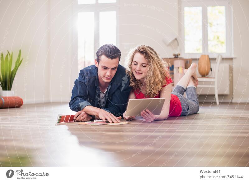 Young couple in new home lying on floor with tablet choosing from color sample select choose selecting twosomes partnership couples flat flats apartment