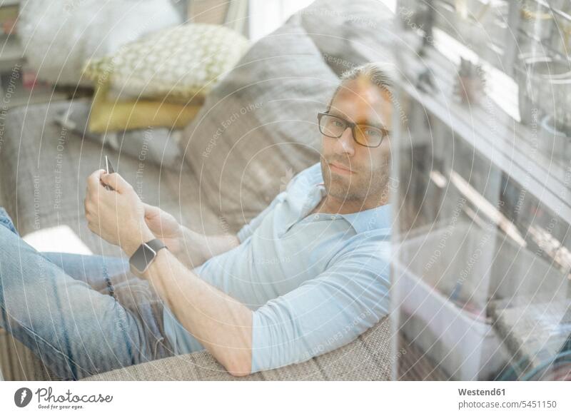 Man relaxing on couch using cell phone settee sofa sofas couches settees mobile phone mobiles mobile phones Cellphone cell phones man men males relaxed